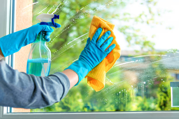 Hands cleaning glass window with spray bottle and yellow cloth